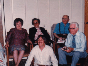 Older adults and a young man gathered in a cozy living room, highlighting family history and genealogy moments.