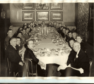 Elegant family gathering around a long dinner table, vintage black and white photo, classic celebration scene, historical family event, Genealogy Gary.